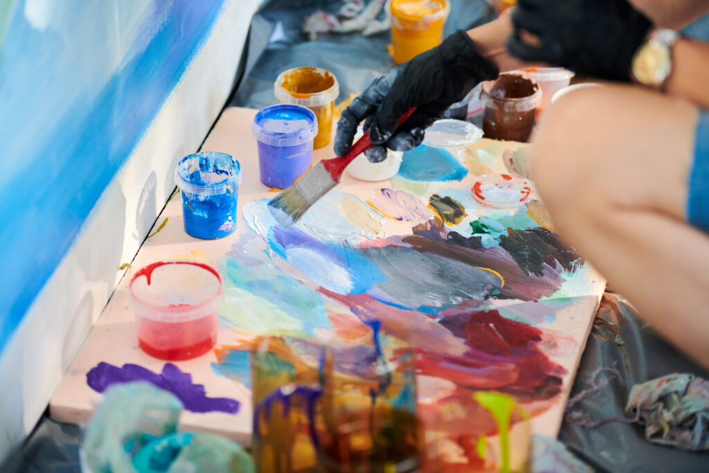 Artist hand in black gloves holds paint brush and choose color from colorful palette at art festival