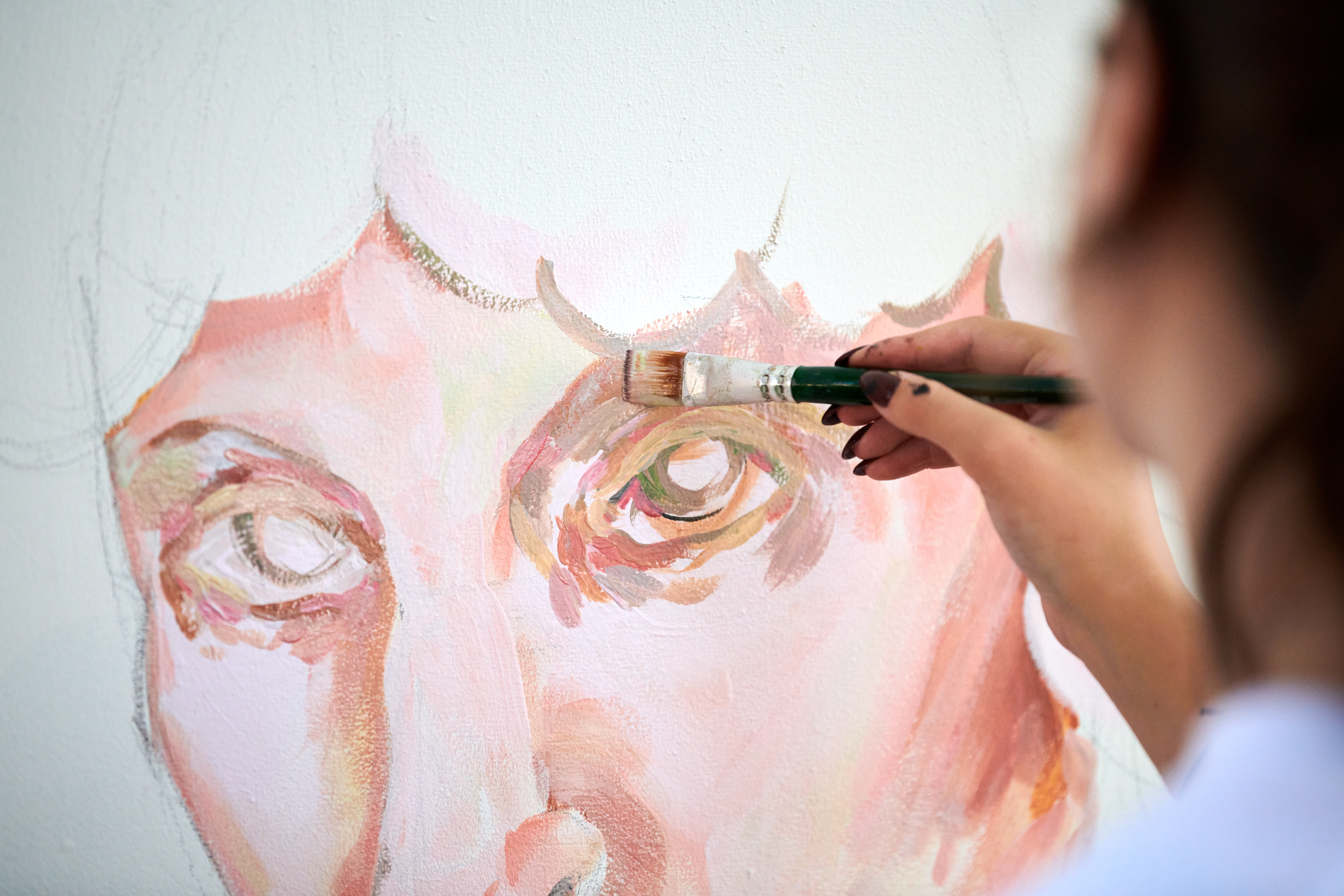 Young girl artist draws with paint brush man portrait on white canvas at art painting festival